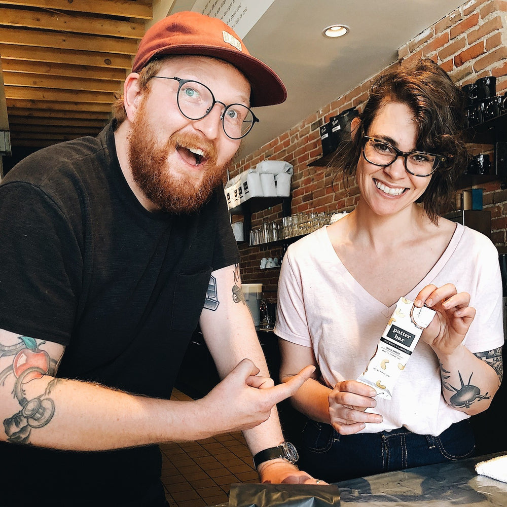 Image of two Thump Coffee Roasters employees in Denver holding a Coconut Cashew Patterbar smiling