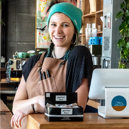 Image of a smiling barista in Denver with a variety box of Patterbars