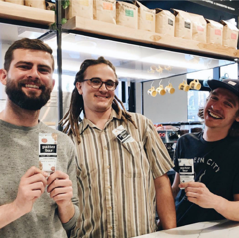 Image of smiling baristas holding Fruit Nut Seed, Coconut Cashew, and Blueberry Lemon Patterbars at Huckleberry Roasters on Wazee in Denver
