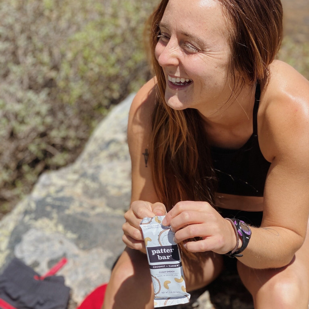 Image of a hiker holding a Coconut Cashew Patterbar taking a break during a hike in Colorado